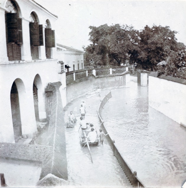 Photograph, view of a canal from an upper storey showing a boat on a flooded path